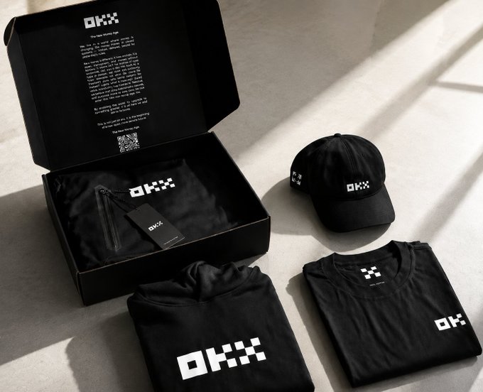 An unboxing of a merchandise package featuring a black 'OKX' branded cap, t-shirt, and hoodie presented alongside the open box and packaging materials.