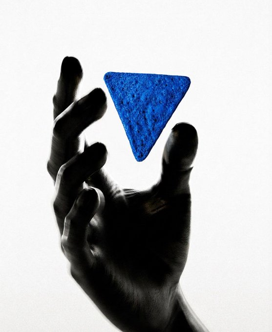 A silhouetted hand reaches up toward a blue triangular chip against a pale background, visually echoing the "$BLUECHIP" token's symbolic branding. The composition conveys aspiration and pursuit, aligning with the post's message of aiming for the 100M milestone.