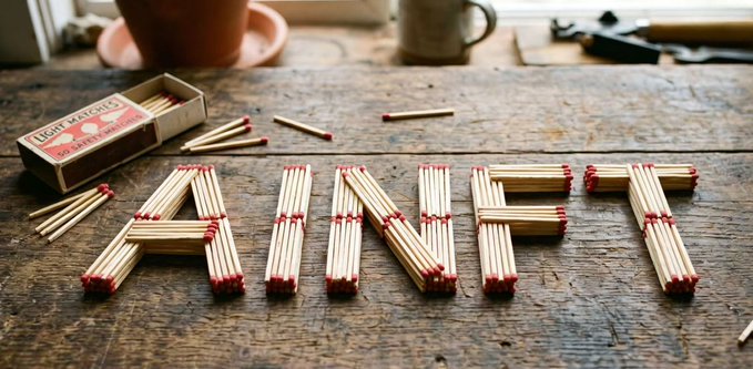 The word "AINFT" is creatively arranged using matches on a wooden surface, with a "LIGHT MATCHES" box nearby. The image visually reinforces the post's theme about AINFT exploring autonomous AI agents in the Web3 space, using the structural assembly of matches as a metaphor for how software agents can build and coordinate complex decentralized workflows.