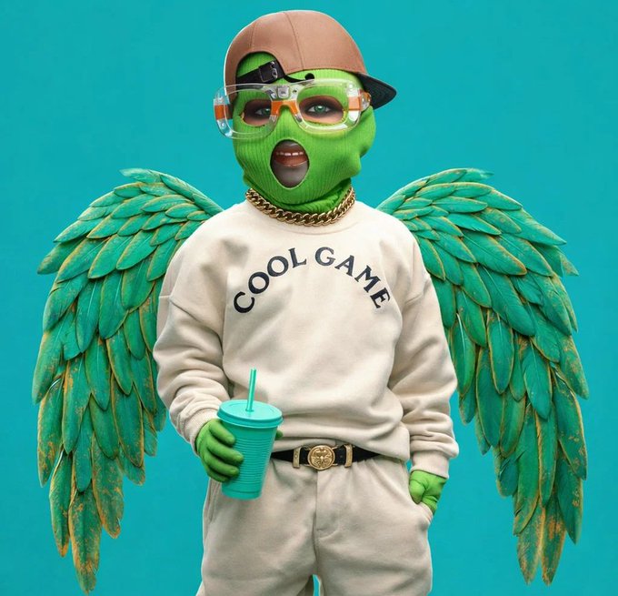 A stylized 3D character with green skin, teal wings, and a backward cap wears a sweatshirt reading 'COOL GAME' while holding a cup.