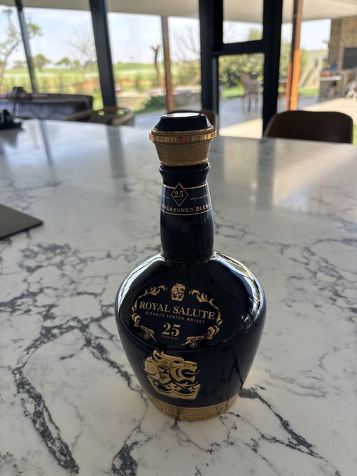A bottle of Royal Salute 25 Year Old "Treasured Blend" Blended Scotch Whisky sits on a marble countertop, gifted as a thank-you from a Palantir investor junior colleague who bought $100K worth of Palantir shares at $18. The Korean caption celebrates fellow long-term Palantir investors, suggesting a celebratory toast before returning to the investment battle tomorrow.