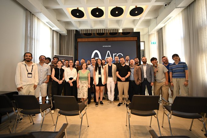 A group photo of around 25 attendees gathered at an event for Wintermute's "Arc" program, standing together in a modern conference room with the event branding displayed on a screen behind them. The image appears to accompany a post about strategies for accessing Arcus Perps, highlighting community networking and engagement within the Wintermute ecosystem.