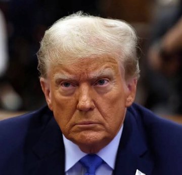 A close-up portrait captures a serious-looking man with blonde hair, wearing a dark blue suit and blue tie, appearing to be in an indoor setting.