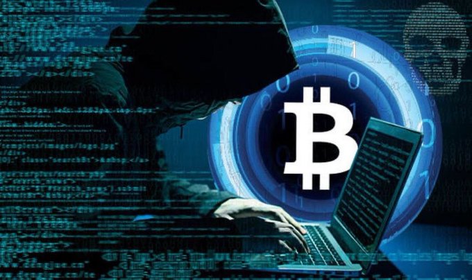 A hooded figure types on a laptop in a dark room, overlaid with digital code, a skull graphic, and a large Bitcoin (₿) logo in the center.