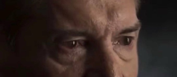 A close-up shot of a man's face shows his eyes filled with emotion, with tears visible, suggesting a somber or sorrowful moment.