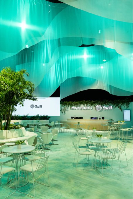 An indoor venue space decorated in teal with white furniture and "Swift" signage displayed on screens.