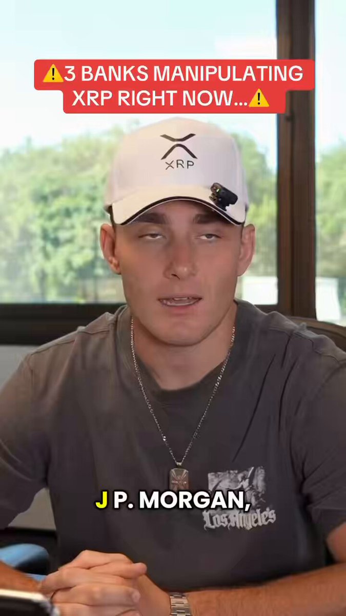 The image shows a man wearing a white baseball cap sitting at a desk, with his hands folded over his lap. The caption of the image reads "THESE 3 BANKS ARE MANIPULATING CRYPTO AND XRP RIGHT NOW... youtu.be/789OeLg2mJU?". This suggests that there is an ongoing discussion or event related to cryptocurrency and banks manipulating it, possibly involving XRP in particular.