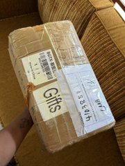 A cardboard shipping package wrapped in packing tape with shipping labels, held by a hand over a striped couch.