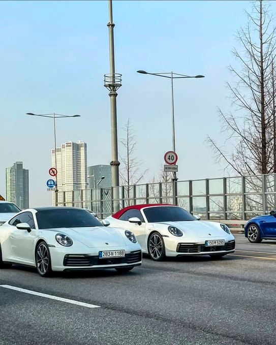 Two white Porsche 911 convertibles parked on a city street, one with a red soft top and one with the top down.