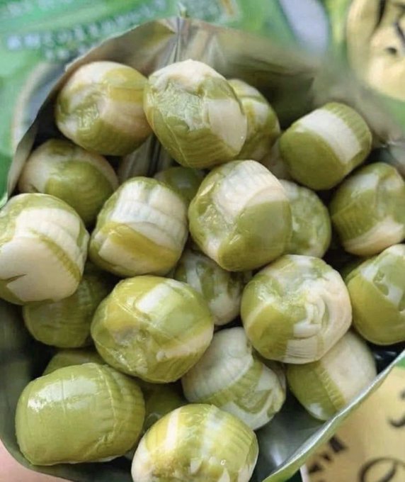 A close-up shot of a package filled with small, round, green and white striped candies wrapped in translucent wrappers, which appear to be a type of traditional Asian sweet.
