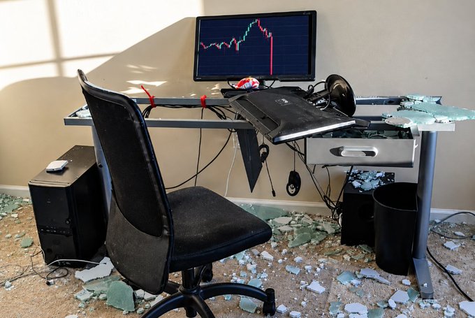 An abandoned, ransacked office with a broken desk, shattered glass on the floor, and a monitor displaying a stock chart showing a sharp red decline.