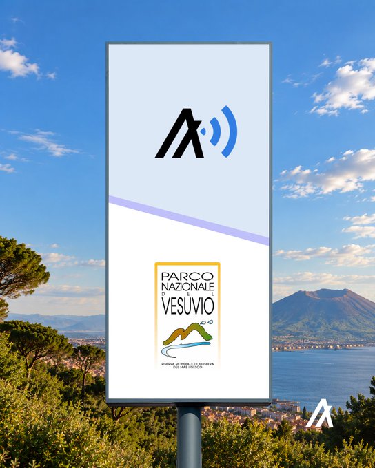 An advertising billboard with a wireless signal logo and the 'Parco Nazionale del Vesuvio' emblem stands against a scenic backdrop featuring a bay and a volcano in the distance.