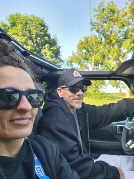 A selfie of a smiling woman wearing sunglasses in the passenger seat of a car, with a man wearing a Cleveland Guardians cap and sunglasses driving.