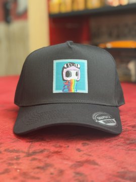 A black snapback cap featuring a square patch with a quirky cartoon robot character spilling rainbow paint, displayed on a red surface.