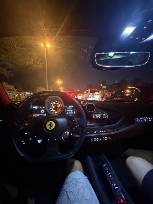 A nighttime view from inside a Ferrari, featuring the iconic prancing horse emblem on the steering wheel alongside an illuminated dashboard display showing "0." The image pairs with the bullish Bitcoin sentiment by visually representing the aspirational "get rich" lifestyle and luxury outcome the post promises to those who stay invested in the crypto super cycle.