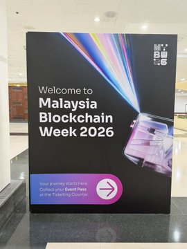 A welcome sign for 'Malaysia Blockchain Week 2026' inviting guests to collect event passes at the ticketing counter.