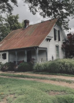 A weathered white farmhouse with a rusted tin roof sits nestled among overgrown greenery and tall trees. The image's peaceful, rural scene perfectly captures the post's sentiment of slowing down and escaping the busy pace of promoting an album.