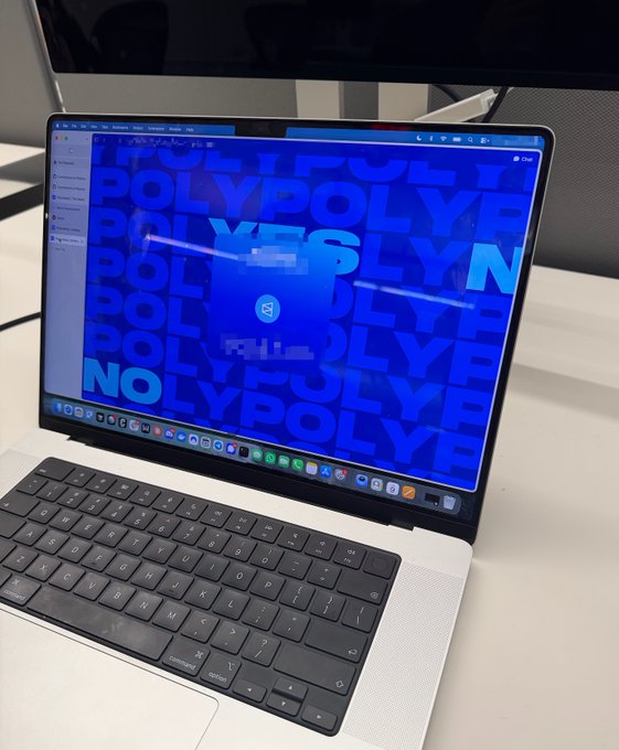 A silver MacBook displays a blue wallpaper covered in repeating "POLY" text with a highlighted "LYN" segment, sitting on a white desk. The image relates to the post by showing the @mustafap0ly desktop wallpaper, which creatively spells out "POLYN" amid the repeated "POLY" branding tied to the $POLY ticker.