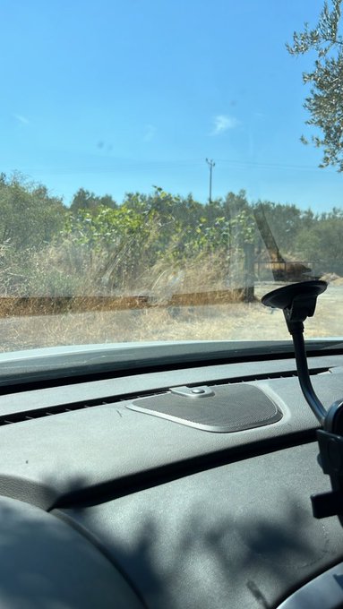 A view from inside a car shows the dashboard, a mounted phone holder, and a rural landscape through the windshield.