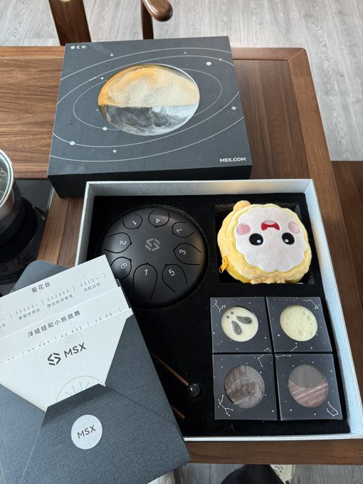 A gift box set featuring a space-themed mooncake box labeled 'MSX' with a planet design on the lid, containing mooncakes and fortune slips with Chinese text including '荔枝烏龍' and '海鹽綠豆小梅觀露'.