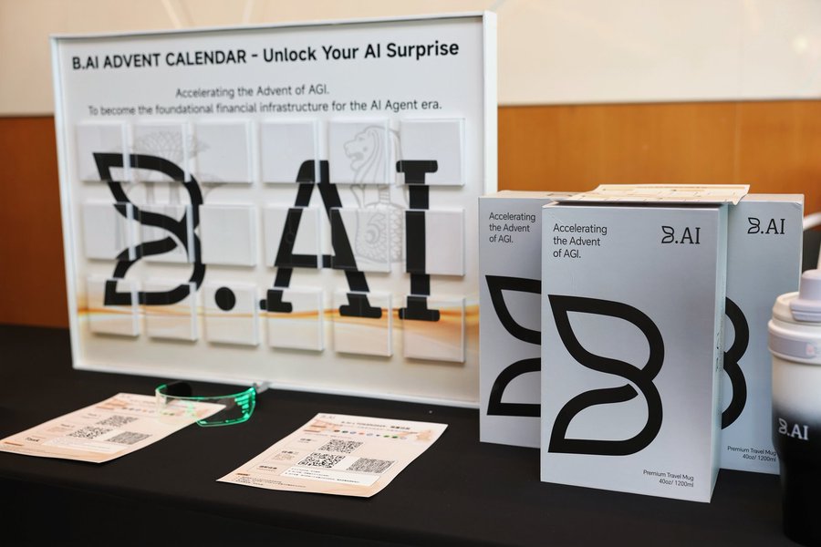 A display table features a "B.AI ADVENT CALENDAR - Unlock Your AI Surprise" with the tagline "Accelerating the Advent of AGI," alongside branded boxes, a tumbler, and informational cards with QR codes. The setup showcases B.AI's presence as a Strategic Partner at the AI Agent Summit in Singapore, where they engaged with fellow builders and pioneers about the future of AI Agent infrastructure.