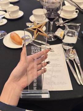 A hand holding a star-shaped '福岡九州 2140' 経済賞 (Economic Award) acrylic trophy at a formal dining table.