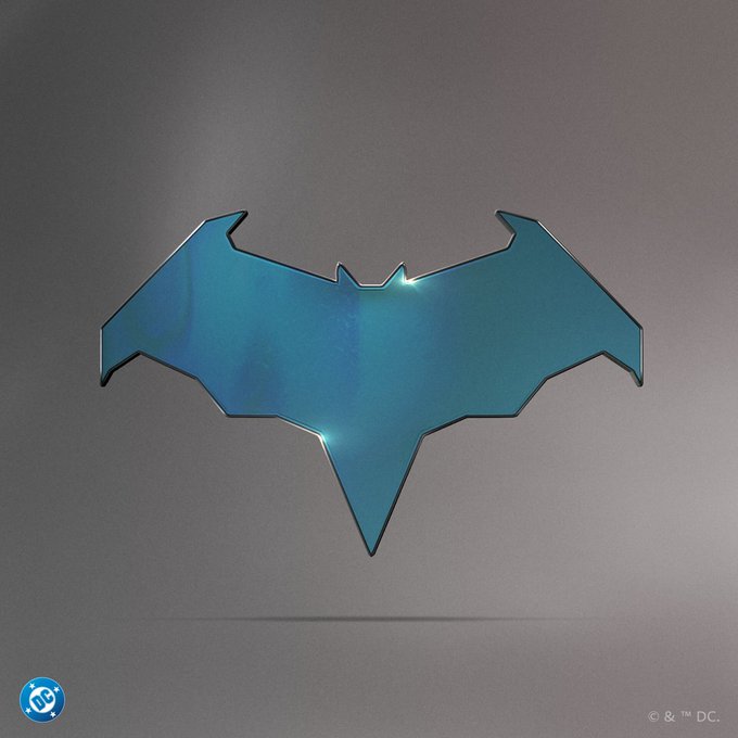 A metallic blue bat-shaped emblem or pin featuring DC Comics branding (© & ™ DC.) displayed against a gradient gray background.