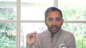 A man with a beard, wearing a gray turtleneck sweater, gestures with his hand while speaking in front of a window with greenery visible outside. The "Pump the turtleneck coin" caption references Chamath Palihapitiya, known for frequently wearing turtlenecks.