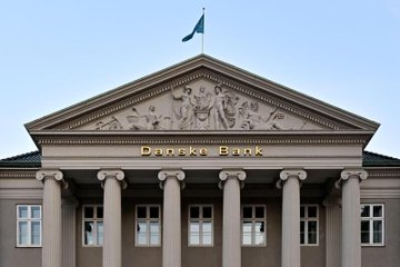 The facade of a classical-style bank building with columns and a pediment, displaying the text 'Danske Bank' below a flag.