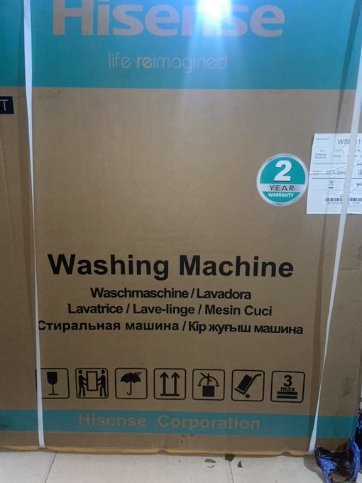 A large Hisense washing machine box with a 2-year warranty label, multilingual product labels, and shipping handling icons sits on a tiled floor. The packaging ties into the post's crypto-to-cash Spenda promotion, suggesting a recent appliance purchase converted through the Spenda service.
