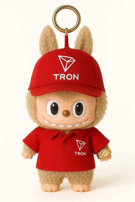 A plush keychain character wearing a red cap and polo shirt featuring the TRON logo and the text "TRON" appears to personify the TRON DAO ecosystem, visually reinforcing the post's announcement about TRON DAO strengthening its sovereign decentralized governance through Super Representatives. The whimsical mascot complements the message highlighting TRON DAO's 30-day network milestones and distributed validation achievements as part of building open, scalable Web3 infrastructure.