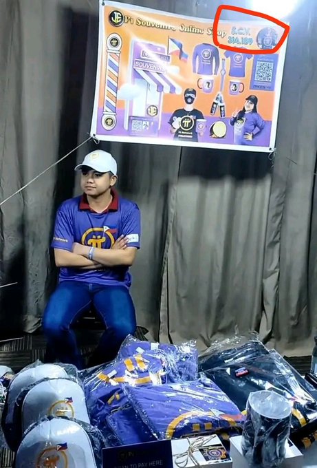 A man in a purple polo shirt and white cap sits behind a display of Pi Network merchandise, with a banner reading "Pi Souvenir Online" showing prices in Philippine pesos and a QR code for GCash payments. The image illustrates the post's argument about unregulated Pi trading, as the vendor appears to be conducting private, cash-based sales of Pi merchandise outside of any formal banking or regulatory channels—exactly the kind of "underground trading" the caption warns against.