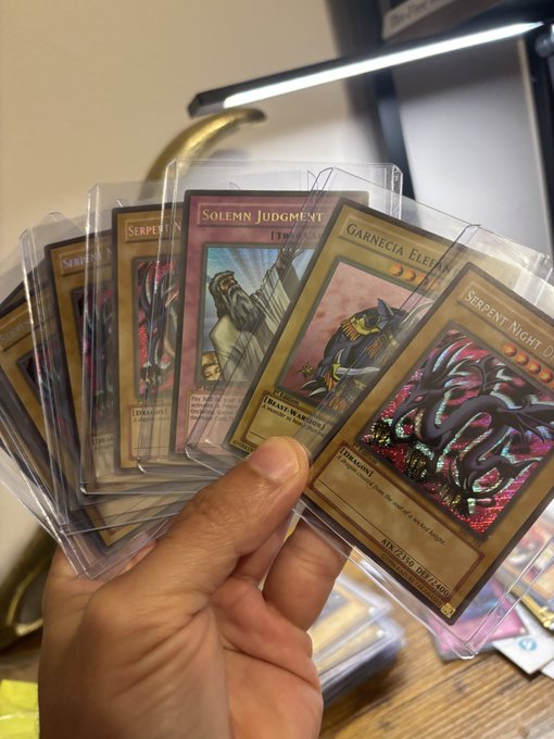 A hand holds up vintage 1st-edition Yu-Gi-Oh cards in protective sleeves, including "Solemn Judgment," "Garnecia Elefant," and "Serpent Night Dragon," all appearing in near-mint condition as noted in the post.
