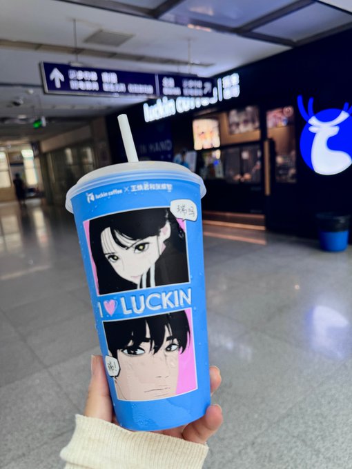 A hand holds a blue Luckin Coffee (瑞幸咖啡) cup featuring anime-style character illustrations and the text "I ♥ LUCKIN." The cup is photographed inside what appears to be a Luckin Coffee store, visible from the illuminated logo in the background.

The image contrasts with the post's excited tone about investments recovering — instead of celebrating financial luck, the caption humorously highlights a moment of "luck" with a Luckin Coffee drink, though the post itself jokingly laments that "getting back to even isn't real profit" (回本不是赚).

Alternatively, the connection is more literal: the brand "LUCKIN" ironically mirrors the poster's surprise at their "lucky" recovery from being trapped in shady stocks (山寨).