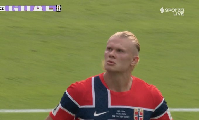Erling Haaland, wearing the Norway national team jersey, looks up with a focused expression on a soccer field, with the text "GUAL" and "SPORTZ LIVE" visible on the broadcast overlay, reinforcing his dominant "AURA" on the pitch.