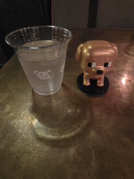 A plastic cup of water with a cute animal design sitting on a wooden table next to a small dog-shaped figurine.
