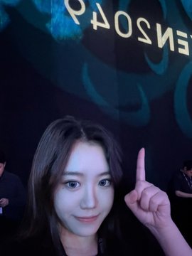 **Event Selfie**: A woman with long hair poses playfully at what appears to be a backstage event, with a person wearing a blue feathered outfit visible behind her near 'ENSOP' signage.