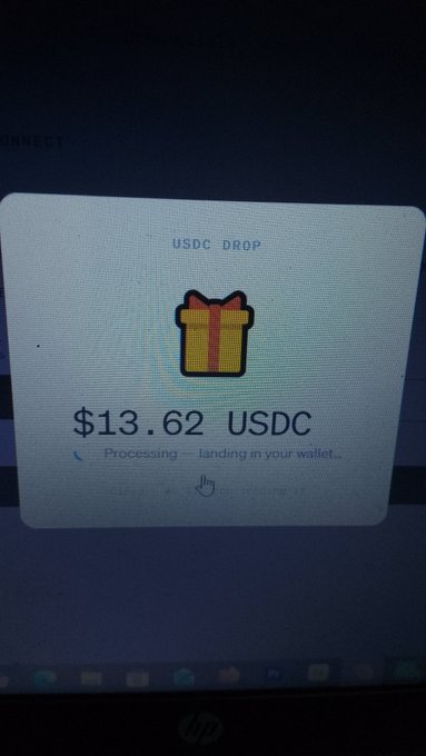 A laptop screen shows a "USDC DROP" notification for $13.62 USDC, featuring a gift box icon and the message "Processing — landing in your wallet...".