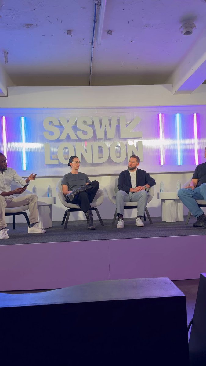 The image shows a group of people sitting around a table, engaged in a discussion about the future of digital economies. The panel consists of four individuals, each sharing their thoughts and opinions on the topic. One person is holding a guitar, suggesting that they might be discussing the role of music or entertainment in the digital age. The setting appears to be an indoor event space with purple walls, which adds a unique ambiance to the conversation.
