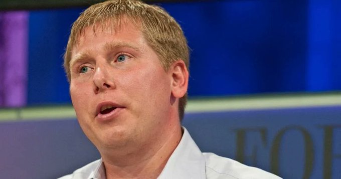 The image likely shows a Digital Currency Group (DCG) executive, possibly Barry Silbert, the CEO, speaking at a public event, relating to the article about a federal judge allowing fraud claims against DCG to proceed in court regarding the Genesis lending arm collapse.