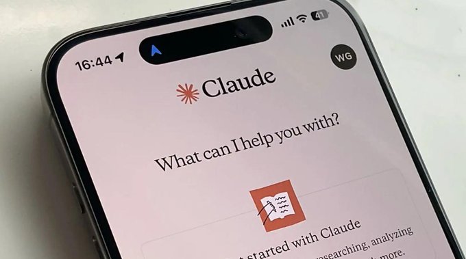 A close-up photograph of an iPhone screen displaying the "Claude" AI assistant app, showing the prompt "What can I help you with?" and a "Get started with Claude" button.