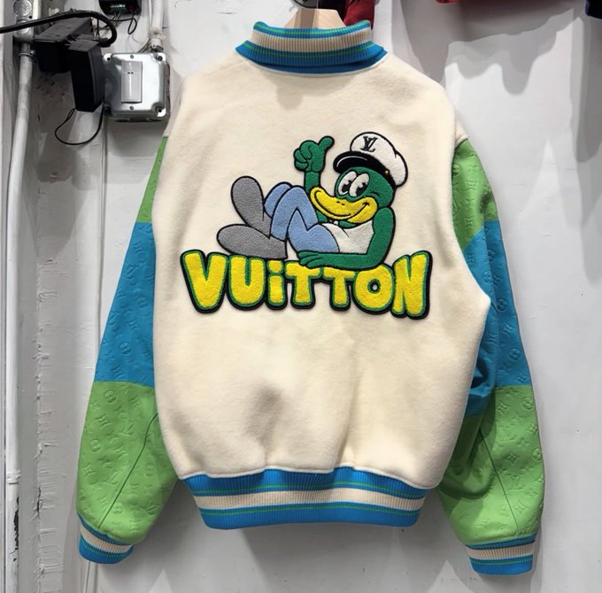 A varsity-style jacket displayed on a hanger featuring a cartoon character wearing a 'Vuitton' cap and green gloves, with 'VUITTON' written in yellow and green on the back.
