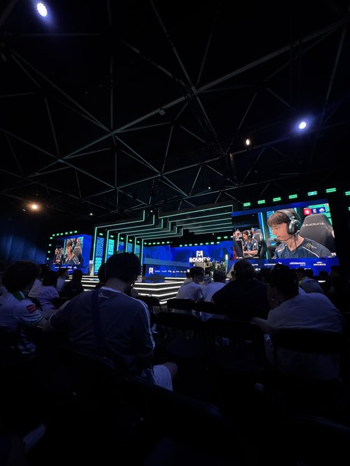 An audience watches a Counter-Strike (CS) esports match on large screens at what appears to be an IEM Rio event, with a young player wearing headphones visible on the broadcast. The humorous caption about being a "Duelbits intern" plays on the idea of hiding in plain sight at a major gaming tournament.