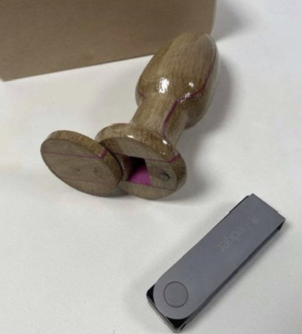 A wooden kendama toy sits next to a Ledger hardware wallet on a white surface, with the "Ledger" branding visible on the device. The image humorously plays on the word "Ledger," connecting a physical "balancing" toy to the post about a new Ledger crypto wallet for gambling funds.