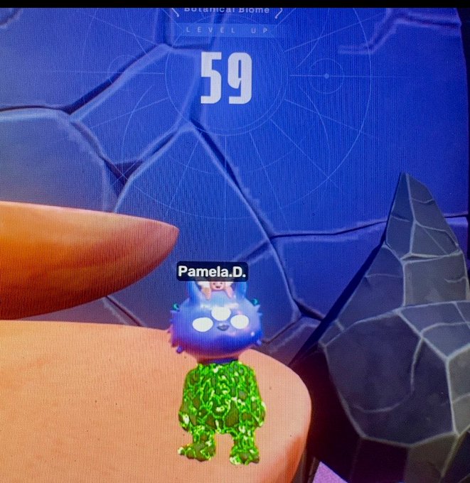 The image shows a character with green skin, standing on an orange platform or rock wall. The character has a name tag that reads "Pamela.D." This character appears to be at level 59 of a video game. There are also other characters in the scene, but they do not seem to have any special significance.