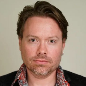 A headshot of Richard Heart, the crypto founder behind HEX and PulseChain, looking directly at the camera with a neutral expression while wearing a patterned shirt and dark jacket, shown in relation to news of his arrest in Turkey by Interpol.