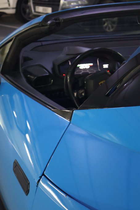 A close-up view of a bright blue sports car, showing the steering wheel and dashboard through the windshield in what appears to be a parking garage.