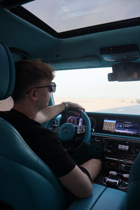 A man wearing sunglasses drives a luxury Mercedes-Benz SUV with a teal leather interior and starlight headliner, his hand resting on the steering wheel as the infotainment screen displays a navigation map. The "GM if you GM" caption suggests a playful nod to General Motors, highlighting the high-end European craftsmanship of the Mercedes as a point of automotive bragging rights.