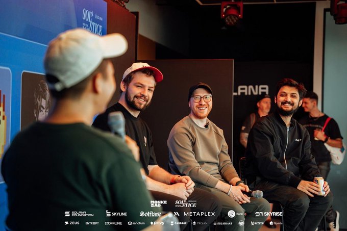 Three men sit on a panel at a tech or esports event, smiling while speaking into a microphone, with sponsor logos including Holozone, Skyline, Solflare, Metaplex, and Skyrise visible at the bottom of the frame.