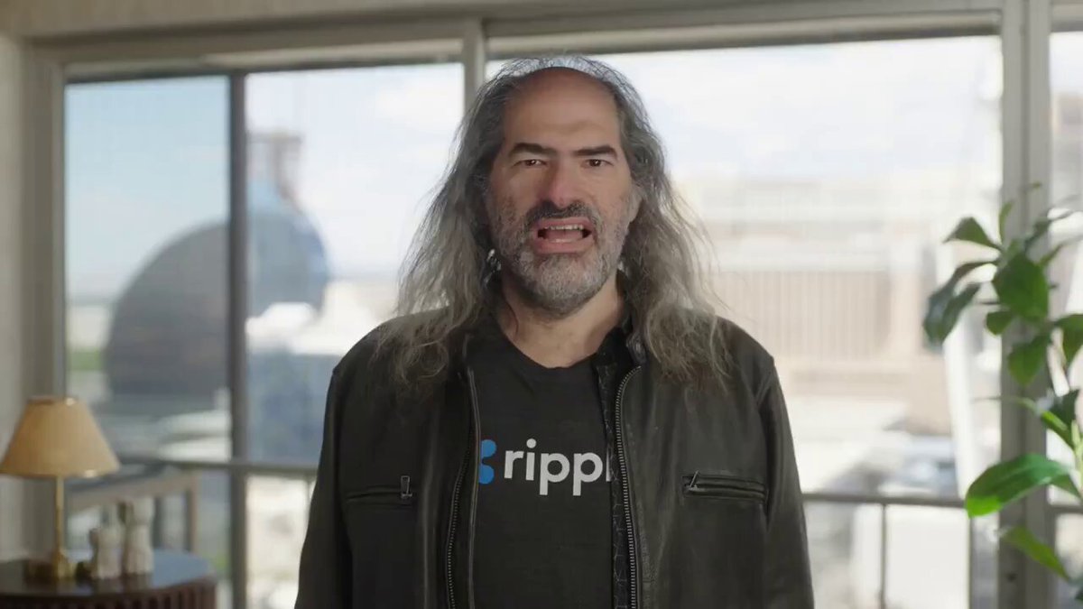 The image features a man with long hair wearing a black jacket standing in front of a window. He has a serious expression as he looks directly at the camera, possibly posing for a photo or participating in an interview. The background includes a desk with various items on it and a potted plant nearby. The post that accompanies this image is titled "BOOOOOOOOOOOOOOOOM Ripple CTO @Joel Katz says enterprises are already using the $XRPL Ledger to tokenize real-world assets. Next: tokenized securities, money market funds, stocks, repos, and loans."